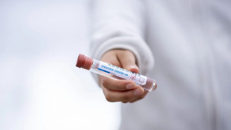Mão segurando frasco com amostra de coronavírus; vacina de Covid-19 está em fase de testes